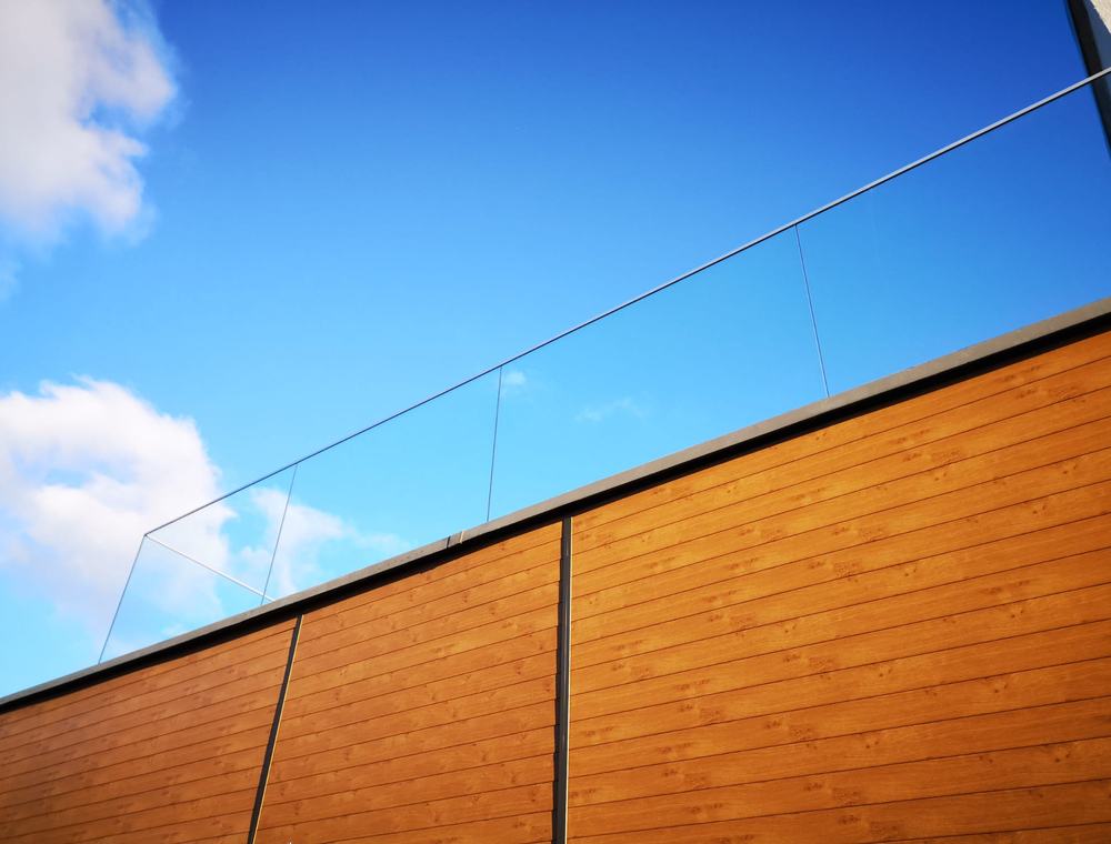 Detal elewacji aluminiowej w dekorze drewna przy balustradzie szklanej