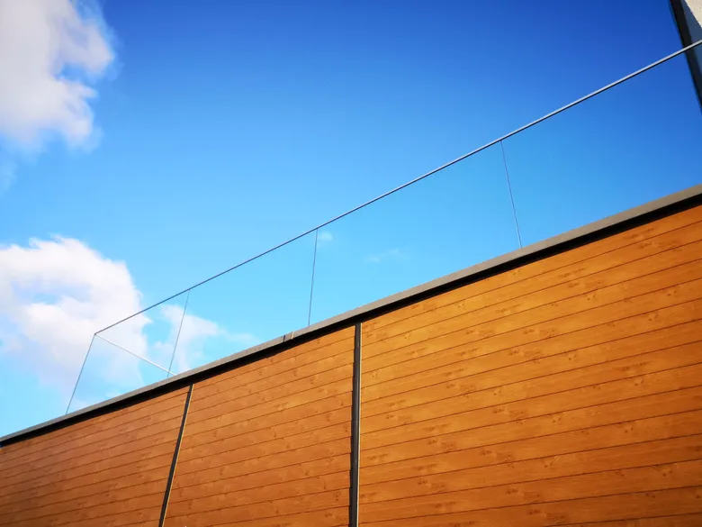 Detal elewacji aluminiowej w dekorze drewna przy balustradzie szklanej